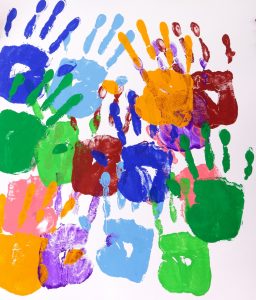 Painted handprints with art and craft equipment on a school table.